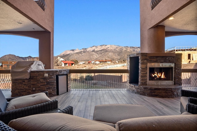 view of patio with a warm lit fireplace, a mountain view, and area for grilling