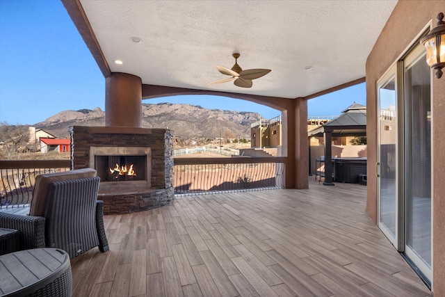 wooden deck featuring an outdoor stone fireplace, a mountain view, a ceiling fan, and a gazebo