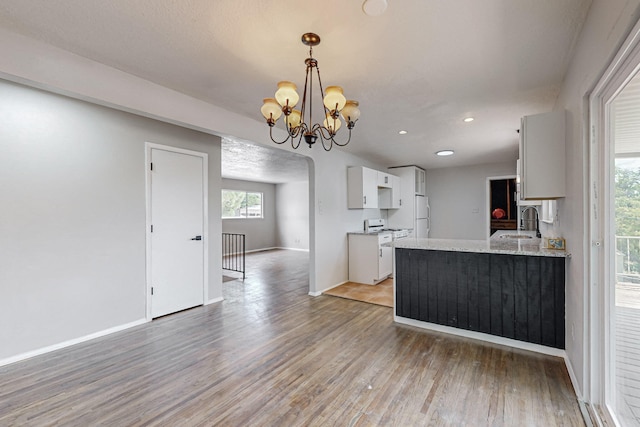 kitchen with light hardwood / wood-style floors, an inviting chandelier, hanging light fixtures, light stone countertops, and white cabinets