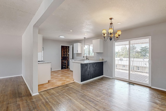 kitchen featuring a notable chandelier, pendant lighting, kitchen peninsula, sink, and white cabinets