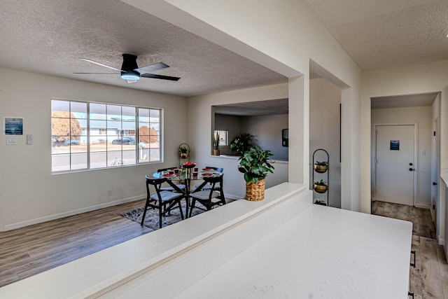 dining area featuring a textured ceiling, wood finished floors, a ceiling fan, and baseboards