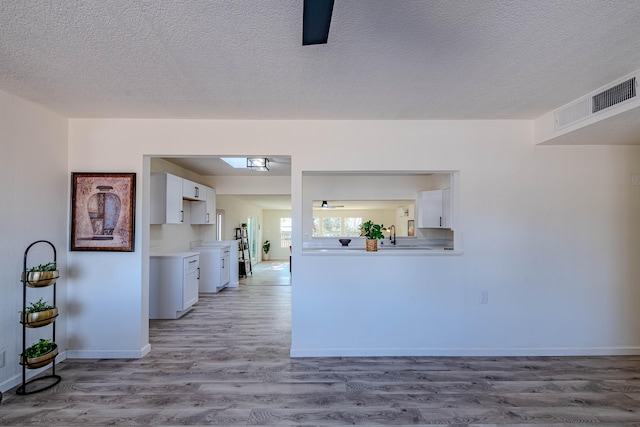 kitchen featuring light countertops, visible vents, white cabinets, wood finished floors, and baseboards