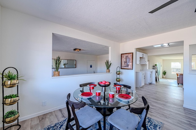 dining space featuring baseboards, a textured ceiling, and light wood finished floors