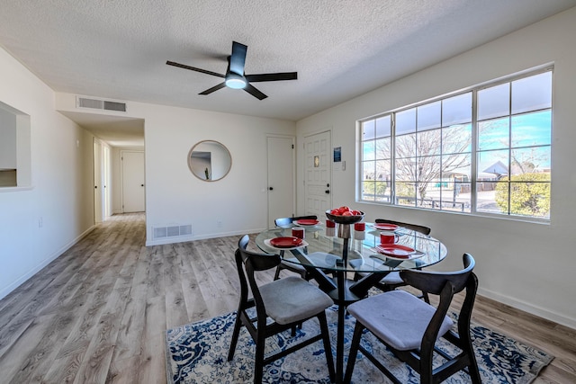 dining room with baseboards, a textured ceiling, visible vents, and wood finished floors