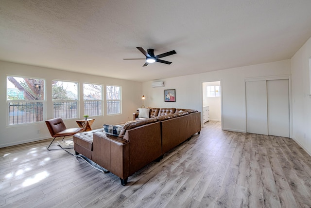 living area with a ceiling fan, an AC wall unit, light wood-style flooring, and a textured ceiling