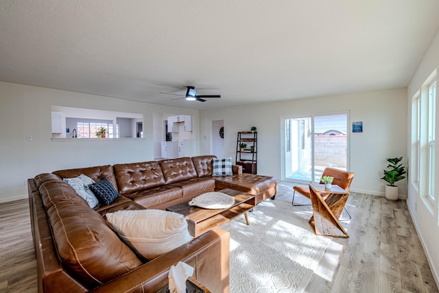 living area featuring a healthy amount of sunlight, light wood finished floors, baseboards, and a ceiling fan