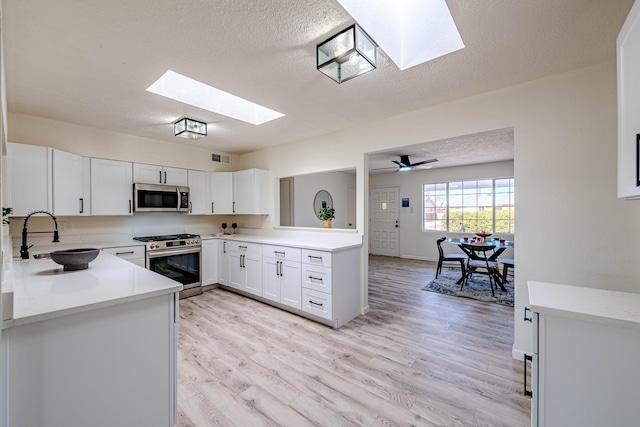 kitchen featuring stainless steel appliances, a sink, white cabinets, light countertops, and light wood finished floors