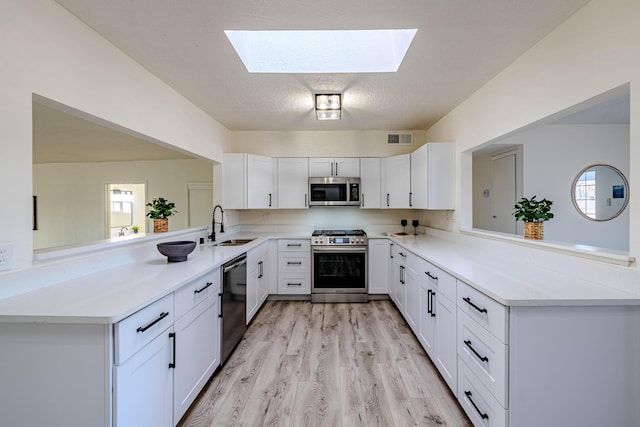 kitchen with a skylight, visible vents, appliances with stainless steel finishes, a peninsula, and a sink