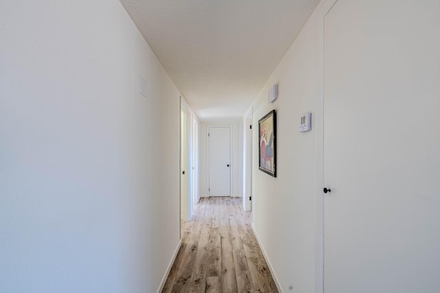 corridor featuring light wood-style flooring and baseboards