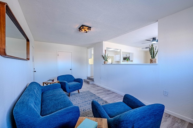 living area with visible vents, baseboards, a textured ceiling, and light wood finished floors