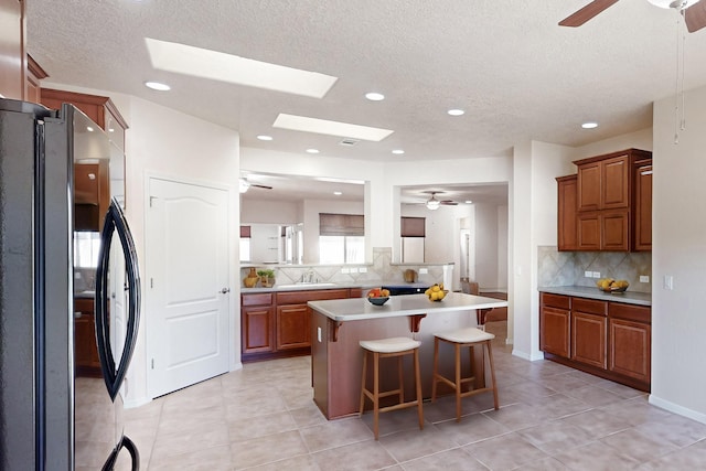 kitchen featuring a kitchen island, black refrigerator, tasteful backsplash, sink, and a breakfast bar area