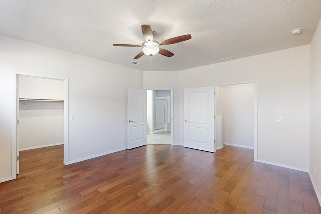 unfurnished bedroom with dark wood-type flooring, ceiling fan, a spacious closet, and a closet