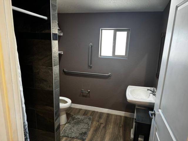 bathroom featuring toilet, a shower, hardwood / wood-style floors, and sink