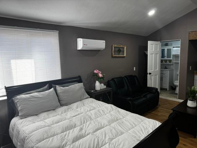 bedroom featuring lofted ceiling, hardwood / wood-style flooring, ensuite bathroom, and a wall mounted air conditioner