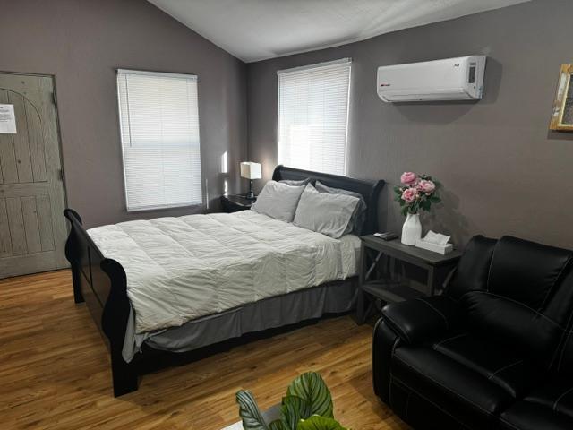 bedroom with a wall unit AC, lofted ceiling, and hardwood / wood-style flooring