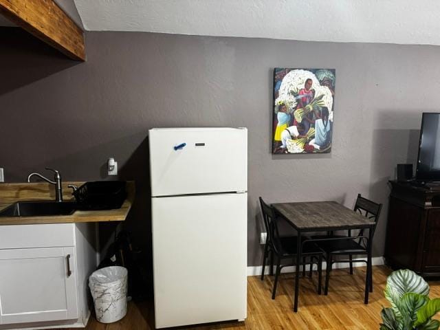 kitchen with white refrigerator, light hardwood / wood-style flooring, white cabinets, and sink