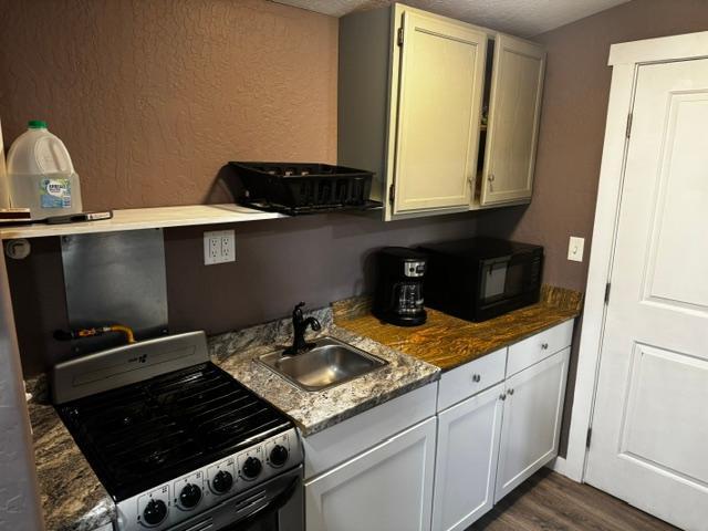 kitchen with stainless steel gas range, dark stone countertops, white cabinets, and sink