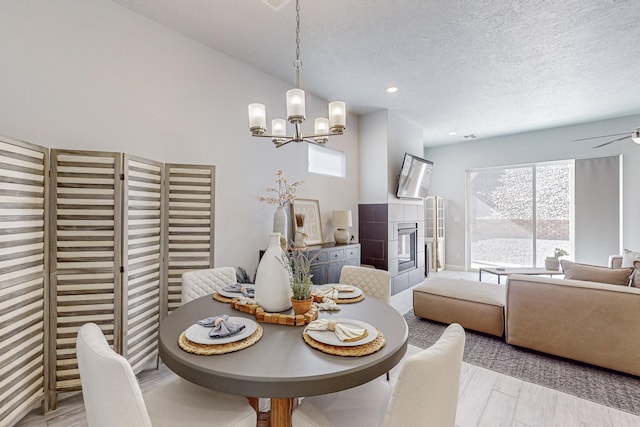 dining room with ceiling fan with notable chandelier, a fireplace, a textured ceiling, and light wood-type flooring