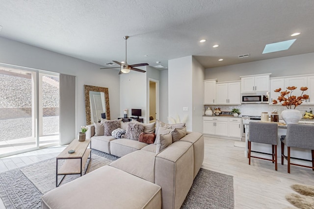 living room with ceiling fan, light hardwood / wood-style floors, and a textured ceiling