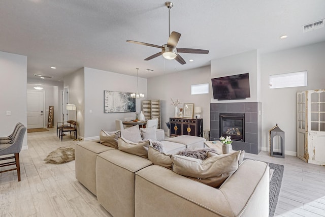 living room featuring a tiled fireplace, ceiling fan, and light hardwood / wood-style floors