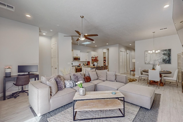 living room featuring ceiling fan with notable chandelier and light wood-type flooring