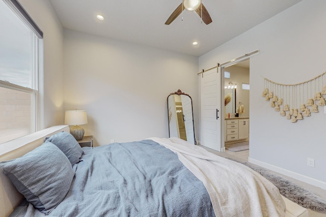 carpeted bedroom with a barn door, ceiling fan, and ensuite bath