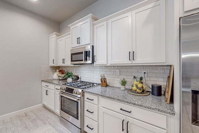 kitchen with light stone counters, tasteful backsplash, stainless steel appliances, and white cabinets