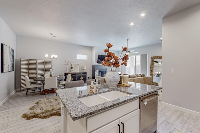 kitchen featuring dishwasher, an island with sink, sink, white cabinets, and a textured ceiling