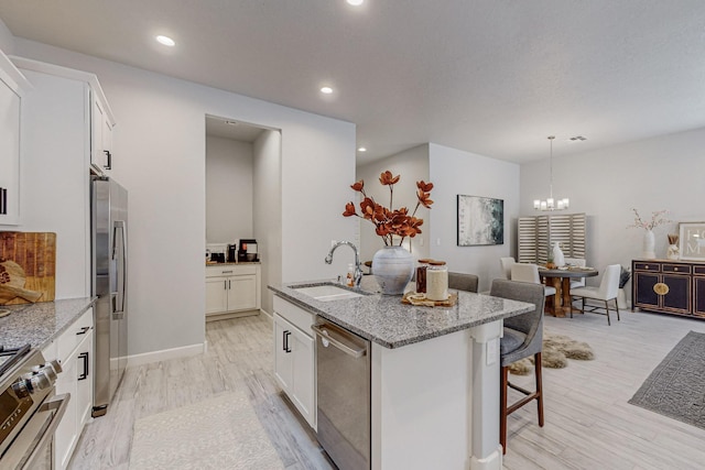 kitchen featuring appliances with stainless steel finishes, an island with sink, sink, white cabinets, and light stone counters