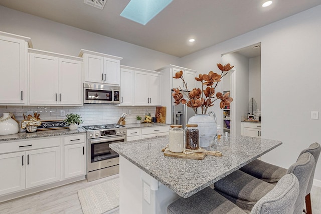 kitchen with light stone countertops, an island with sink, white cabinets, and appliances with stainless steel finishes