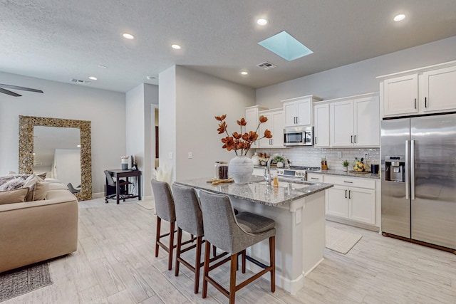 kitchen featuring white cabinetry, light stone counters, a kitchen island with sink, and stainless steel appliances