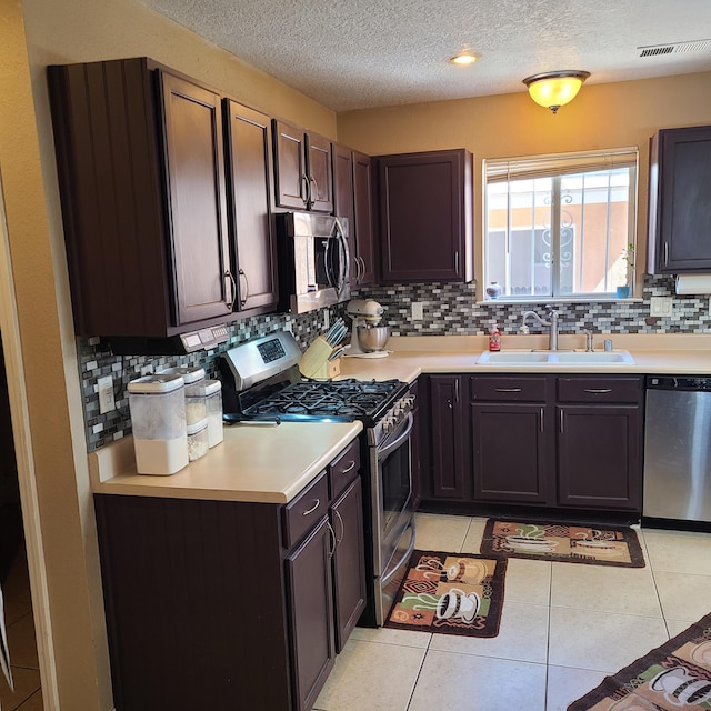 kitchen featuring sink, light tile patterned floors, stainless steel appliances, dark brown cabinetry, and decorative backsplash