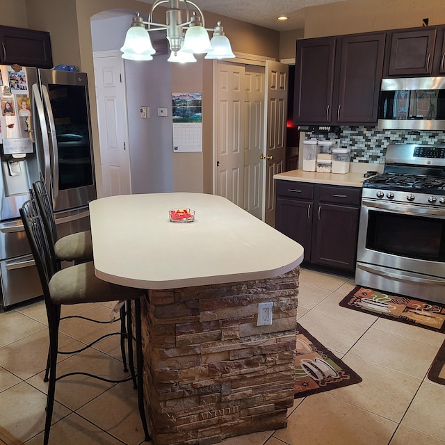 kitchen featuring light tile patterned floors, decorative light fixtures, dark brown cabinets, and stainless steel appliances