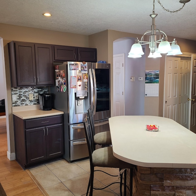 kitchen with hanging light fixtures, backsplash, stainless steel fridge, and dark brown cabinetry