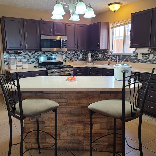 kitchen featuring light tile patterned flooring, appliances with stainless steel finishes, pendant lighting, sink, and a kitchen breakfast bar