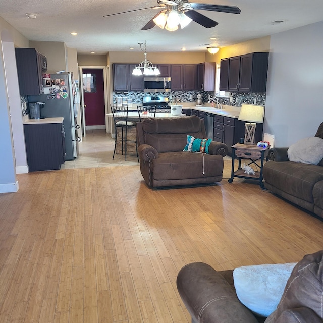 living room featuring ceiling fan with notable chandelier, sink, light hardwood / wood-style floors, and a textured ceiling