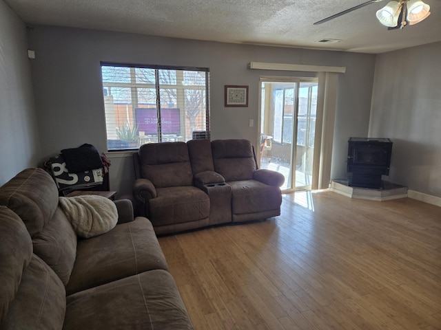 living room featuring plenty of natural light, a wood stove, a textured ceiling, and light hardwood / wood-style flooring