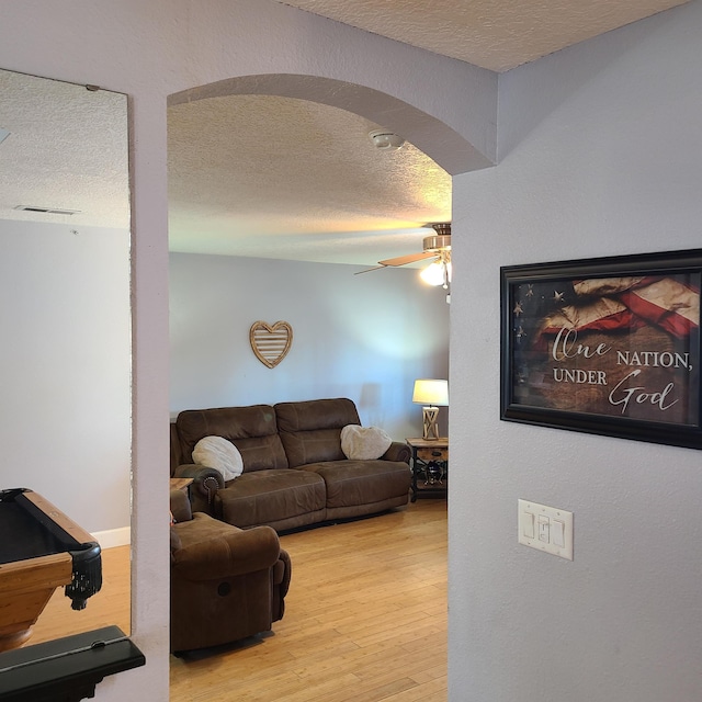 living room featuring ceiling fan, a textured ceiling, and light wood-type flooring