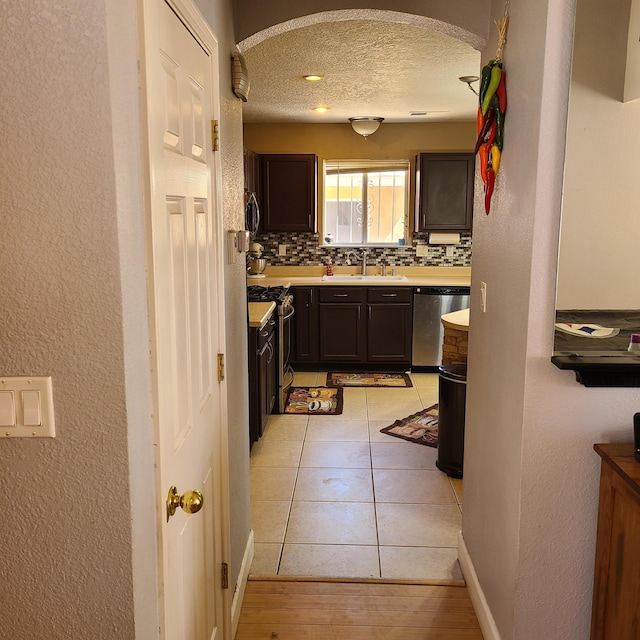 kitchen with light tile patterned flooring, dark brown cabinetry, sink, appliances with stainless steel finishes, and backsplash