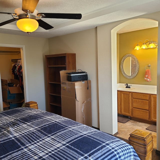 tiled bedroom with sink, a walk in closet, a textured ceiling, a closet, and ceiling fan