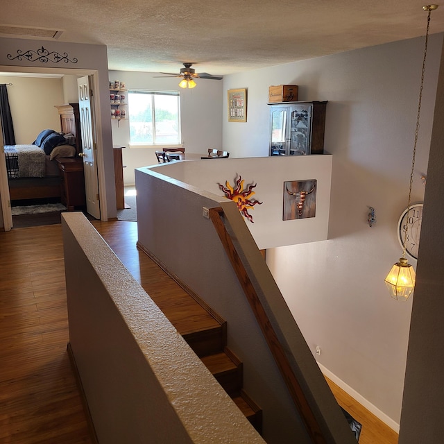 stairway featuring wood-type flooring, a textured ceiling, and ceiling fan