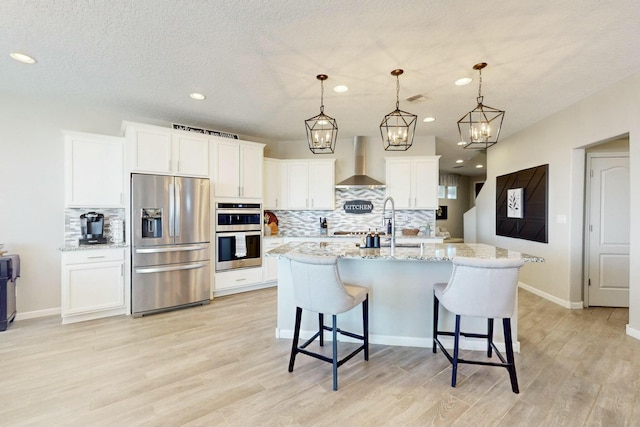 kitchen featuring stainless steel appliances, pendant lighting, backsplash, and wall chimney range hood