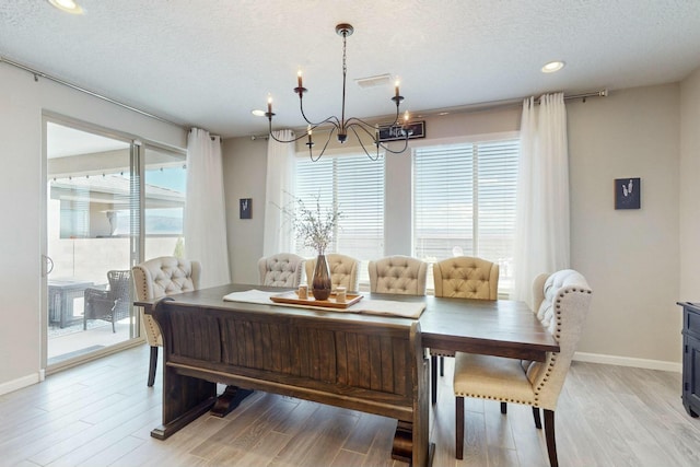 dining space with light hardwood / wood-style floors, a textured ceiling, and an inviting chandelier