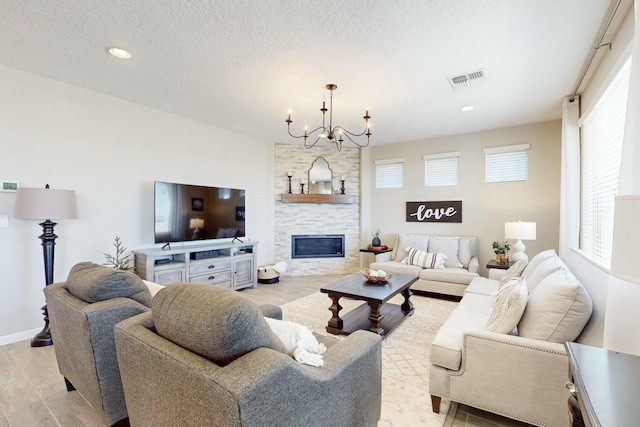 living room with a textured ceiling, light wood-type flooring, a tiled fireplace, and an inviting chandelier