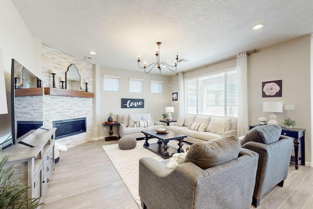 living room featuring a textured ceiling, a fireplace, a chandelier, and light hardwood / wood-style floors