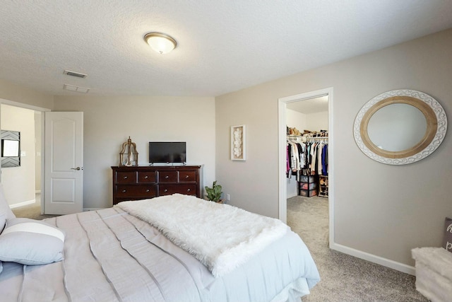 bedroom featuring a walk in closet, a closet, light colored carpet, and a textured ceiling