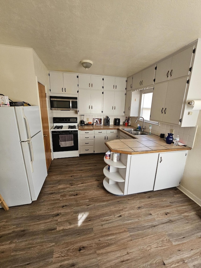 kitchen with white fridge, white cabinetry, tile counters, dark wood-type flooring, and gas range