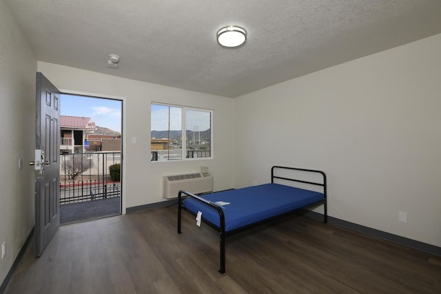 bedroom with a textured ceiling, dark wood-type flooring, access to exterior, and a wall unit AC