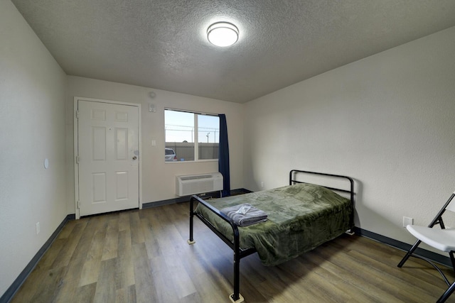 bedroom featuring a wall mounted AC, a textured ceiling, and hardwood / wood-style floors