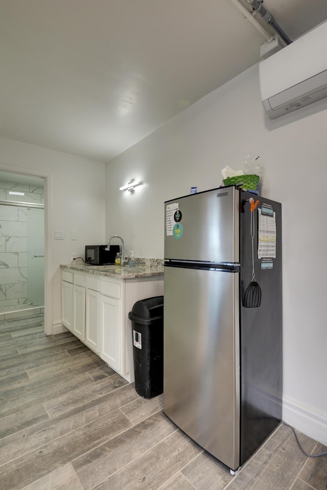 kitchen featuring an AC wall unit, stainless steel refrigerator, sink, white cabinets, and light stone counters